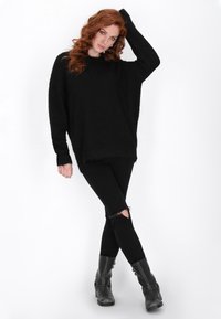 Pullover oversized nero e peloso con maniche lunghe, abbinato a jeans skinny neri strappati e stivali neri alla caviglia con dettagli in metallo.