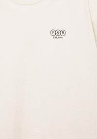 T-shirt blanc à col rond avec un petit logo noir "P & B" à l'intérieur de trois cercles et "EST. 1991" imprimé en dessous sur la poitrine.