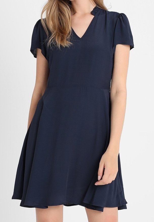 Femme portant une robe bleu marine à manches courtes avec un décolleté en V et une jupe légèrement évasée, sur un fond uni.