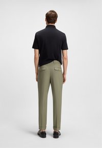 Crna polo majica i maslinaste hlače tailored fit, s stražnjim džepovima i crnim cipelama. Jednostavan dizajn s čistim linijama.