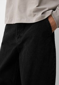 Black denim pants with a mid-rise design and straight cut. Material shows slight texture, with visible stitching along the seams.