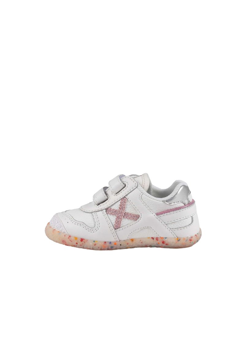 Zapatilla blanca con dos cintas de velcro, acentos plateados y una suela texturizada con motas coloridas. En el lateral tiene un detalle bordado en rosa.