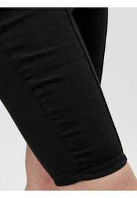 Capri in denim nero con un design aderente, caratterizzati da una superficie liscia, cuciture a macchina e un orlo che si posiziona appena sopra il ginocchio.