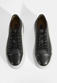 Schwarze Ledersneaker mit einer strukturierten Oberfläche, verfügen über eine glatte Lederzehenkappe, schwarze Schnürsenkel und eine weiße Gummisohle.