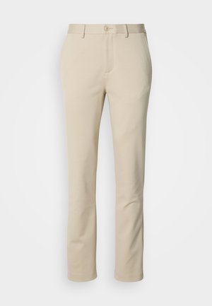 Beżowe bawełniane spodnie z prostymi nogawkami, zapinane na guzik, z płaskim przodem. Materiał ma gładką fakturę i minimalne detale.