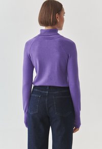 Pull en col roulé violet avec un col côtelé, manches ajustées, assorti à un jean en denim foncé doté de poches arrière et d'une coupe droite.