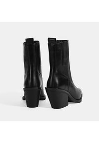 Bottines en cuir noir avec un bout pointu, des panneaux latéraux élastiques et un talon empilé. Texture lisse avec des coutures détaillées le long des seams.