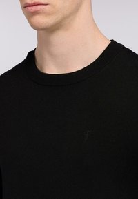 Černá pletená mikina s kulatým výstřihem, s nenápadnou vyšívanou logem na hrudi a hladkou texturou.