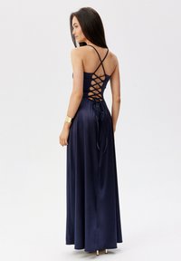 Dlouhá námořnická saténová šaty s křížovým detailem na zádech a stuhou na zavázání. Obsahuje tenké ramínka a splývavý design.