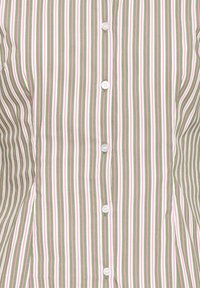 Chemise boutonnée avec des rayures verticales vertes, blanches et roses, montrant une vue rapprochée de la partie avant.