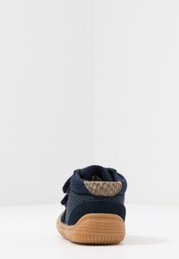 Modré textilní tenisky s strukturovanou zadní částí a uzavřením na suchý zip. Gumová podešev v světlé hnědé barvě. Perforovaný design pro prodyšnost.