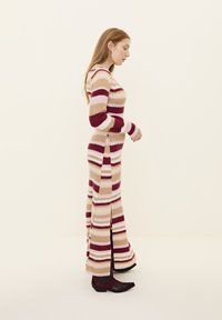 Rochie maxi tricotată cu dungi, cu mâneci lungi, având dungi în nuanțe de roz pal, crem și burgund; cu deschideri laterale; asortată cu botine negre până la gleznă.