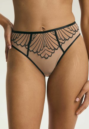 High-waist sheer nude panties with black scallop embroidery worn by a standing person with hands resting near hips.