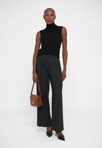 Zwarte coltrui, grijs gestreepte wijd uitlopende broek, zwarte puntige hakken en een bruine schoudertas met gouden accenten.