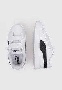 Sneakers bianchi con accenti neri, caratterizzati da una superficie testurizzata, due cinturini in Velcro, punta arrotondata e suola in gomma. Logo Puma visibile all'interno.