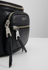 Black leather bag with dual zippered compartments, silver hardware, and branding. Features sleek design and textured surface.