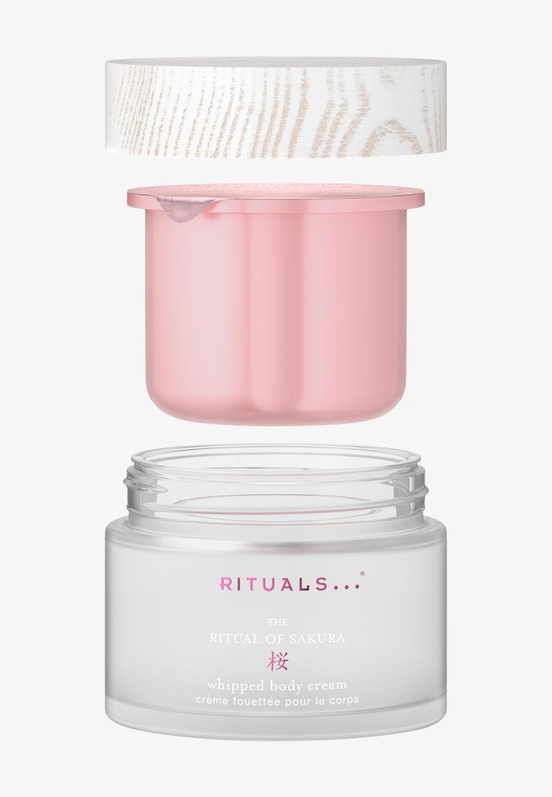 Klar glassbehållare med rosa innerlock och texturerat vitt ytterlock. Etiketten visar varumärke och produktnamn i rosa och vitt.