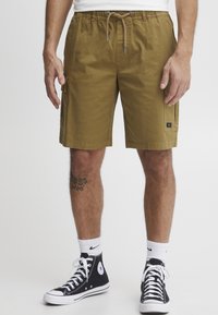 Kaki cargo shorts med elastisk midjebånd og snøring, med sidelommer og teksturert stoff. Båret med svarte joggesko.