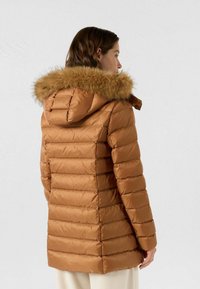 Giacca imbottita marrone con cappuccio rifinito in pelliccia sintetica, design trapuntato e taglio dritto, con cuciture orizzontali e una texture liscia.