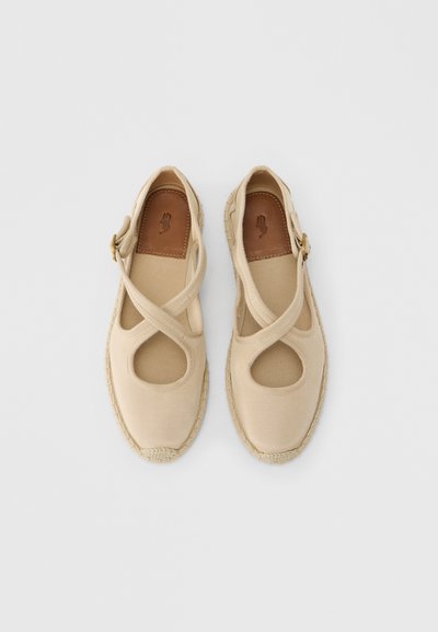 Μπεζ εσπαντρίγιες με διασταυρούμενα λουριά, υφασμάτινο υλικό, ανοιχτές περικοπές και πλεκτή σόλα από τζούτ. Το εσωτερικό πέλμα από δέρμα φέρει ένα λογότυπο με το χέρι.