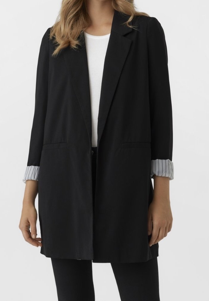 Woman wearing a black blazer with rolled-up pinstriped cuffs over a white shirt and black pants, shown from neck to mid-thigh.