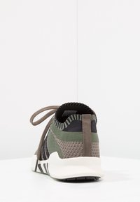 Sportskor med en texturerad stickad ovandel i grön och svart, dragflik vid hälen och en vit mellansula med ett randigt grått yttersuldesign.