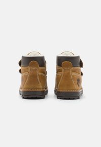 Botas de tobillo de cuero marrón con un suave forro blanco, acentos marrones en contraste y una suela de goma texturizada. Incluye dos correas de gancho y bucle.