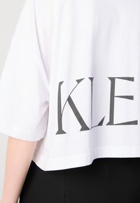 White cropped t-shirt with short sleeves featuring bold black block lettering on the back. Cotton material, smooth texture.