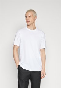 Short-sleeve white cotton t-shirt with a crew neckline, featuring a relaxed fit and smooth texture. Paired with black trousers.