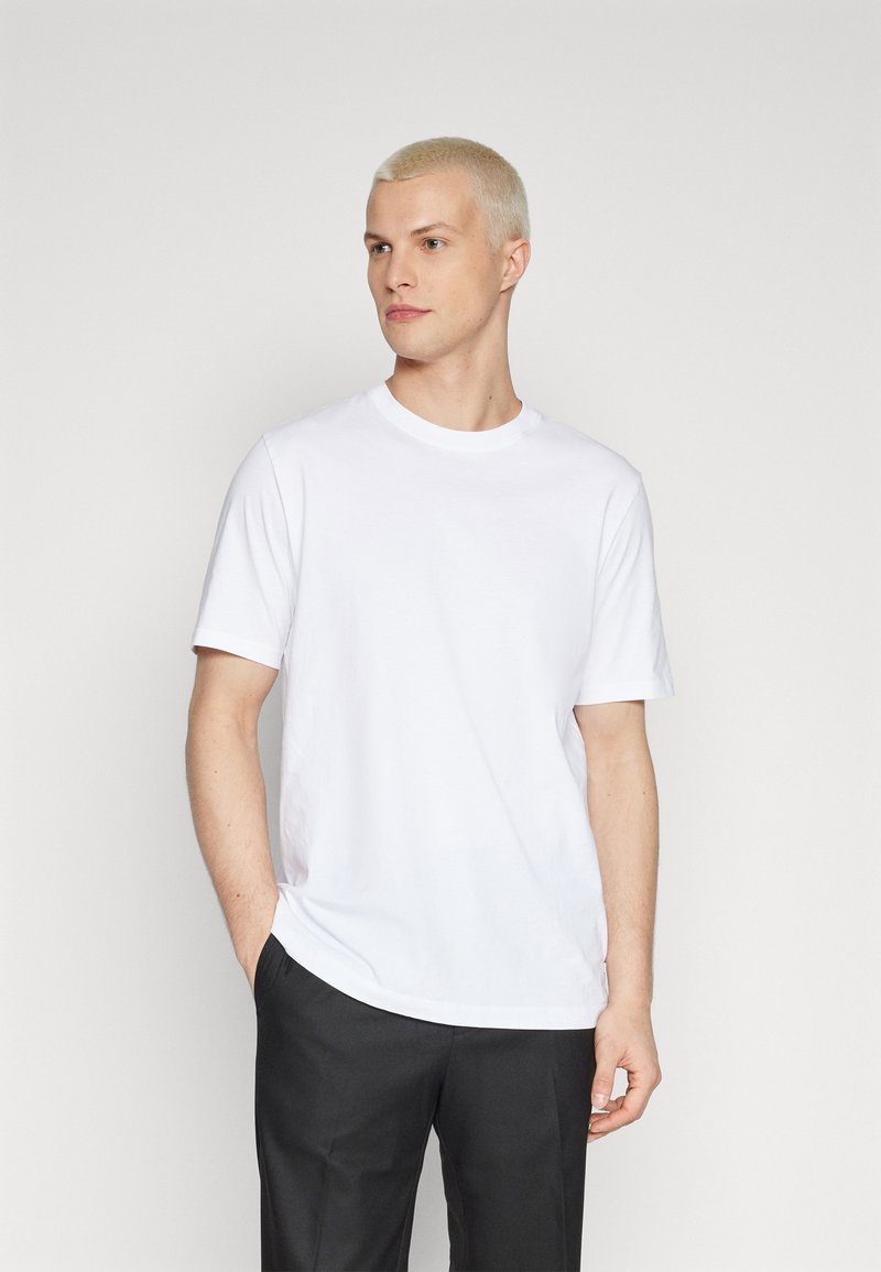 Short-sleeve white cotton t-shirt with a crew neckline, featuring a relaxed fit and smooth texture. Paired with black trousers.