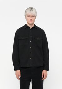 Black shirt featuring a button-up design, two chest pockets, and long sleeves. Made of cotton with a smooth texture.