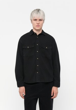 Black shirt featuring a button-up design, two chest pockets, and long sleeves. Made of cotton with a smooth texture.