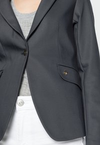 Grå kavaj i slät tyg, med en enkel knappknäppning, två framfickor och en strukturerad grå skjorta under.