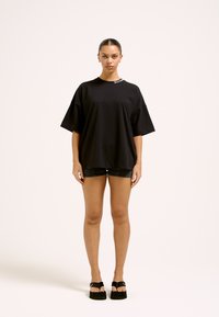 Mustast puuvillast oversize-t-särk, millel on lühikesed varrukad, ümar kaelus ja kaela lähedal asuv brändi logo detail. Komplektis teksapükstega.