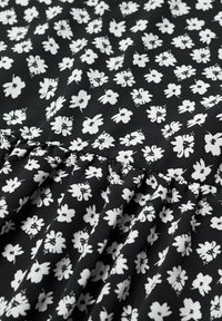 Tissu noir avec un motif floral blanc. Présente de petites fleurs aux dessins variés. Le matériau a une texture douce et lisse avec des plis.