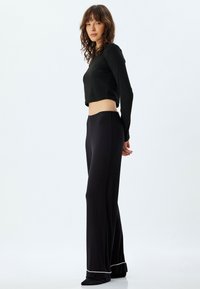 Schwarzes langärmeliges Crop-Top in Kombination mit schwarzen weiten Hosen mit elastischem Bund und weißen Besätzen am Saum. Einfaches, sauberes Design.