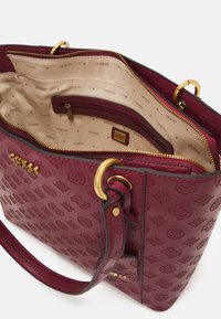 Borsa Guess bordeaux con motivo in rilievo, hardware dorato, apertura con zip e interno foderato in tessuto beige con stampa logo e tasca interna con zip.