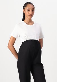 Vit kortärmad t-shirt med ett strukturerat mönster, i kombination med svarta högmidjade byxor med knytdetalj i midjan.