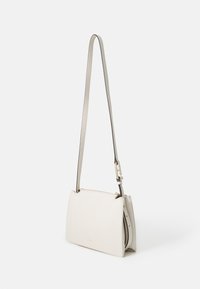 Bílá kožená crossbody taška s texturovaným povrchem, vybavená štíhlým nastavitelným popruhem a zipovým uzávěrem. Minimalistický design s jemným brandingem.