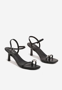 Sandales à talons hauts noires avec des lanières, design à bout carré, fines brides de cheville et accents en métal. Matériau en simili cuir.