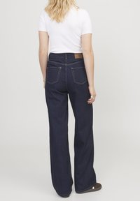 Džíny s vysokým pasem a širokými nohavicemi v tmavě modrém denimovém provedení. Obsahují dvě zadní kapsy a hnědou nášivku na pase. Hladká textura a čisté švy.