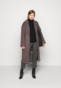 Palton lung din lână gri, cu un croi lejer, rever mari și deschidere frontală. Purtați deasupra unei bluze negre cu guler înalt și a unor pantaloni cu carouri. Botine negre până la gleznă.