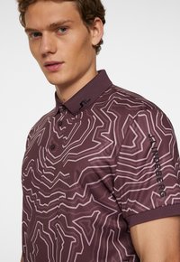 Marinröd polo skjorta med ett geometriskt mönster i ljusare nyanser, med krage, knappar och logotypdetalj på ärmen.