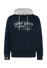 Sudadera marina con forro gris, presentada con texto blanco y azul, cordones ajustables y puños acanalados. Muestra logotipos y coordenadas geográficas.