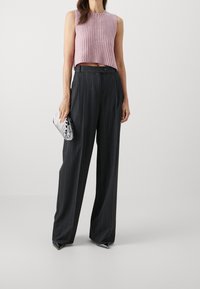 Lichtroze, mouwloze gebreide top gecombineerd met hoog uitgesneden zwarte broek met streepjes en een glanzende zilveren clutch. Lange, vloeiende silhoeet.