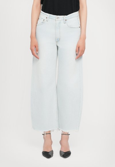 Φαρδιά τζιν σε ανοιχτό μπλε χρώμα από denim, με ψηλή μέση, ξεφτισμένο τελείωμα και πέντε τσέπες, συνδυασμένα με μαύρα παπούτσια με μυτερή μύτη.