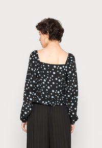 Blusa preta com bolinhas azul claro, decote quadrado, mangas compridas bufantes e bainha com frufrus. Tecido suave e corte descontraído.