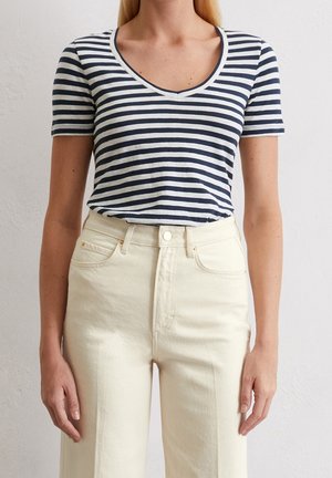 Gestreept T-shirt met een marineblauw en wit patroon, V-hals, korte mouwen, gecombineerd met een beige jeans met hoge taille en zichtbare zakken.