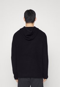 Sweat à capuche noir en maille avec une coupe décontractée, doté d'une grande capuche, de manches longues, d'une texture côtelée et de poches latérales.