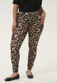 Leggings en imprimé léopard en tissu léger avec une taille élastique ; design ajusté avec des poignets à la cheville. Associés à des chaussures plates noires.